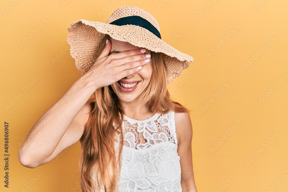 Young caucasian woman wearing summer hat smiling and laughing with hand on face covering eyes for surprise. blind concept. Young caucasian woman wearing summer hat smiling and laughing with hand on face covering eyes for surprise. blind concept.