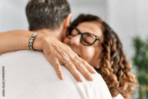 Middle age hispanic couple hugging and smiling happy on marriage proposal. Woman wearing engagement ring on finger at home.