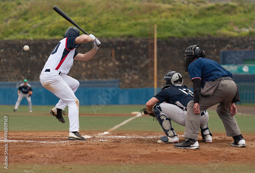 Players playing baseball while standing on field, baseball pitcher throwing ball to batter watched by umpire and catcher