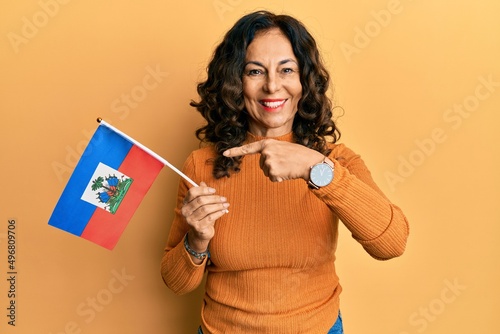 Middle age hispanic woman holding haiti flag smiling happy pointing with hand and finger