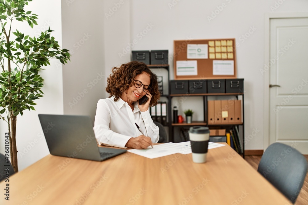 Middle age hispanic woman talking on the smartphone working at office