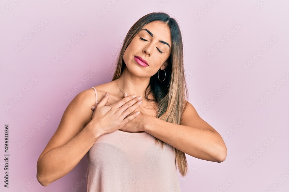 Young hispanic woman wearing casual sleeveless t shirt smiling with hands on chest, eyes closed with grateful gesture on face. health concept. Young hispanic woman wearing casual sleeveless t shirt smiling with hands on chest, eyes closed with grateful gesture on face. health concept.