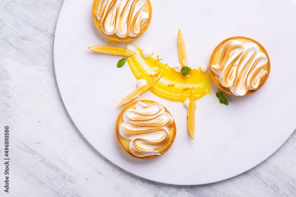 Appetizing lemon tartlets with meringue served on a white plate - obrazy, fototapety, plakaty 