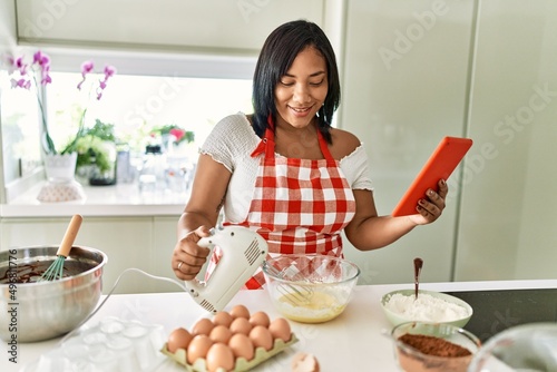 Hispanic brunette woman preparing cake looking at online recipe at the kitchen