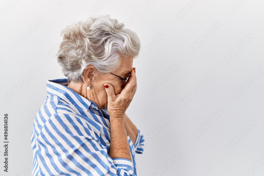 Senior woman with grey hair standing over white background with sad expression covering face with hands while crying. depression concept.