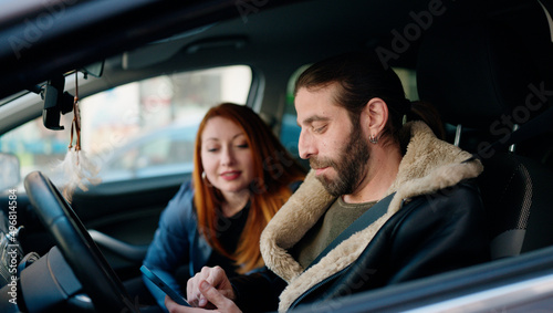 Man and woman couple using smartphone sitting on car at street