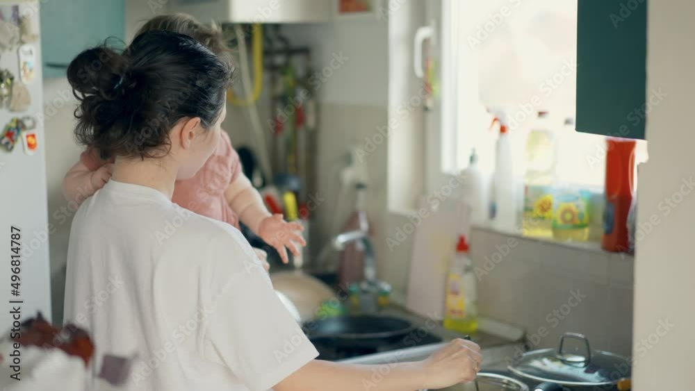 The mother is cooking dish is spoiled by an infant in her arms in the kitchen. Burned porridge. Housewife multitasking at home. The mother is cooking dish is spoiled by an infant in her arms in the kitchen. Burned porridge. Housewife multitasking at home.