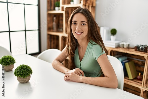 Young hispanic woman smiling confident sitting on table at home
