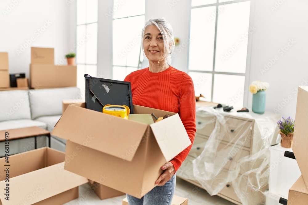 Middle age grey-haired woman smiling confident holding package at new home Middle age grey-haired woman smiling confident holding package at new home