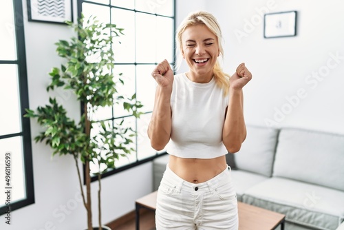 Young caucasian woman standing at living room excited for success with arms raised and eyes closed celebrating victory smiling. winner concept. © Krakenimages.com