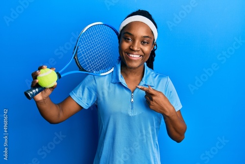 African american woman with braided hair playing tennis holding racket and ball smiling happy pointing with hand and finger © Krakenimages.com