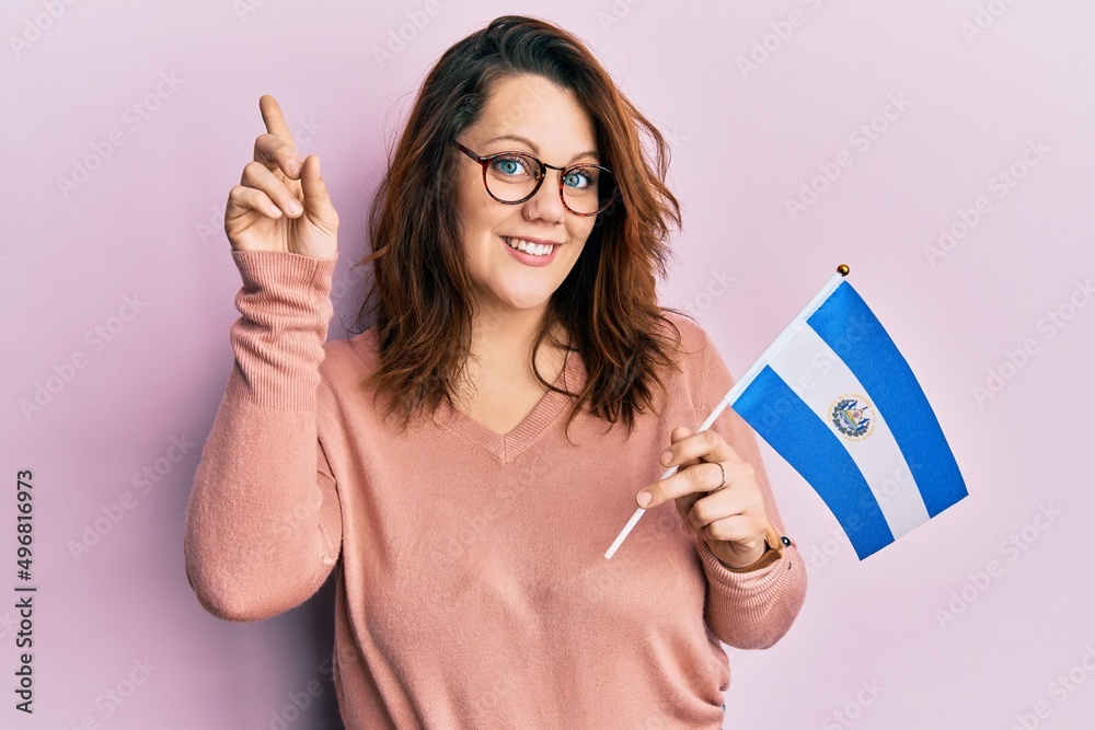 Young caucasian woman holding el salvador flag smiling with an idea or question pointing finger with happy face, number one Young caucasian woman holding el salvador flag smiling with an idea or question pointing finger with happy face, number one