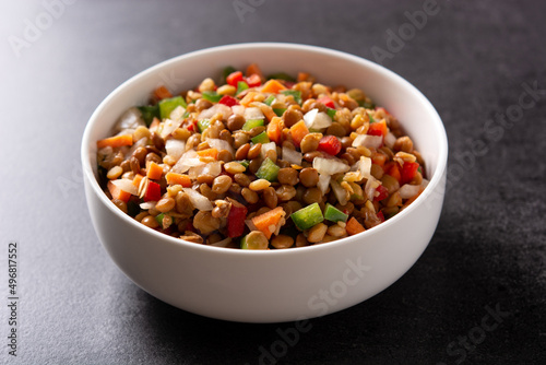 Lentil salad with peppers,onion and carrot in a bowl on black background