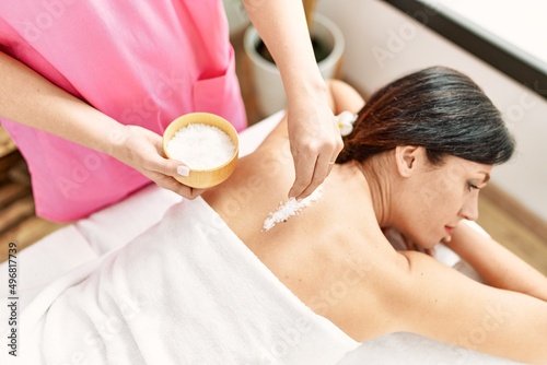 Middle age hispanic woman having salt back massage at beauty center