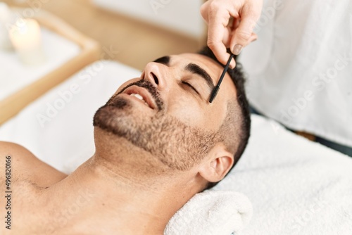 Young hispanic man having eyebrows treatment at beauty center