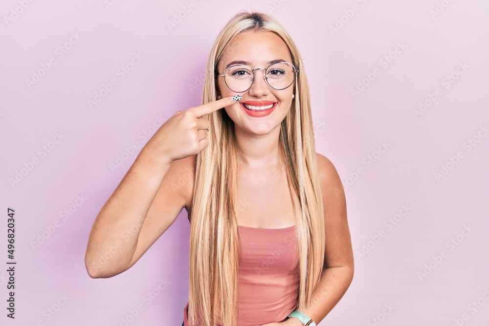 Young blonde girl wearing casual clothes pointing with hand finger to face and nose, smiling cheerful. beauty concept Young blonde girl wearing casual clothes pointing with hand finger to face and nose, smiling cheerful. beauty concept