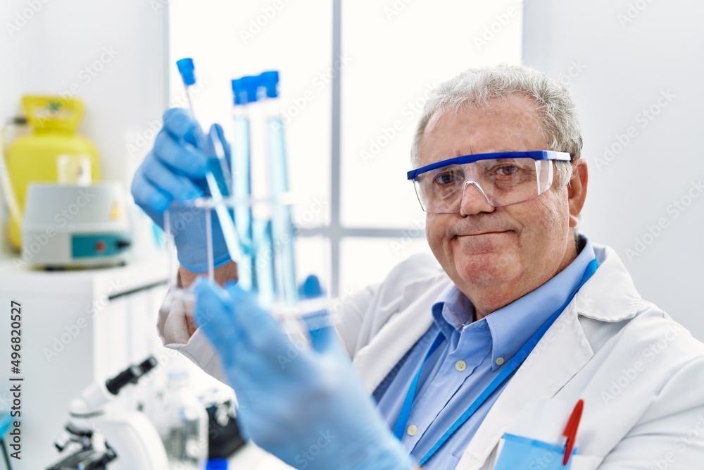 Middle age grey-haired man wearing scientist uniform holding test tube at laboratory Middle age grey-haired man wearing scientist uniform holding test tube at laboratory