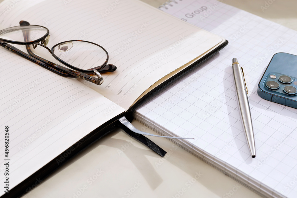 Fototapeta premium Office desk with notebook, pen, mobile phone. Top view at an angle.