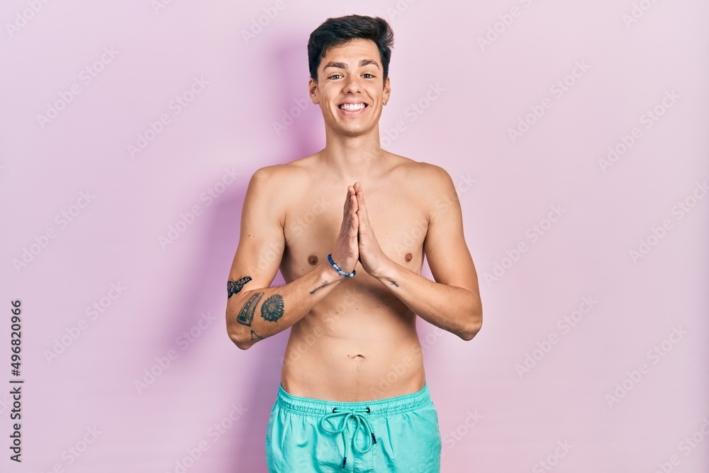 Fototapeta premium Young hispanic man wearing swimwear shirtless praying with hands together asking for forgiveness smiling confident.