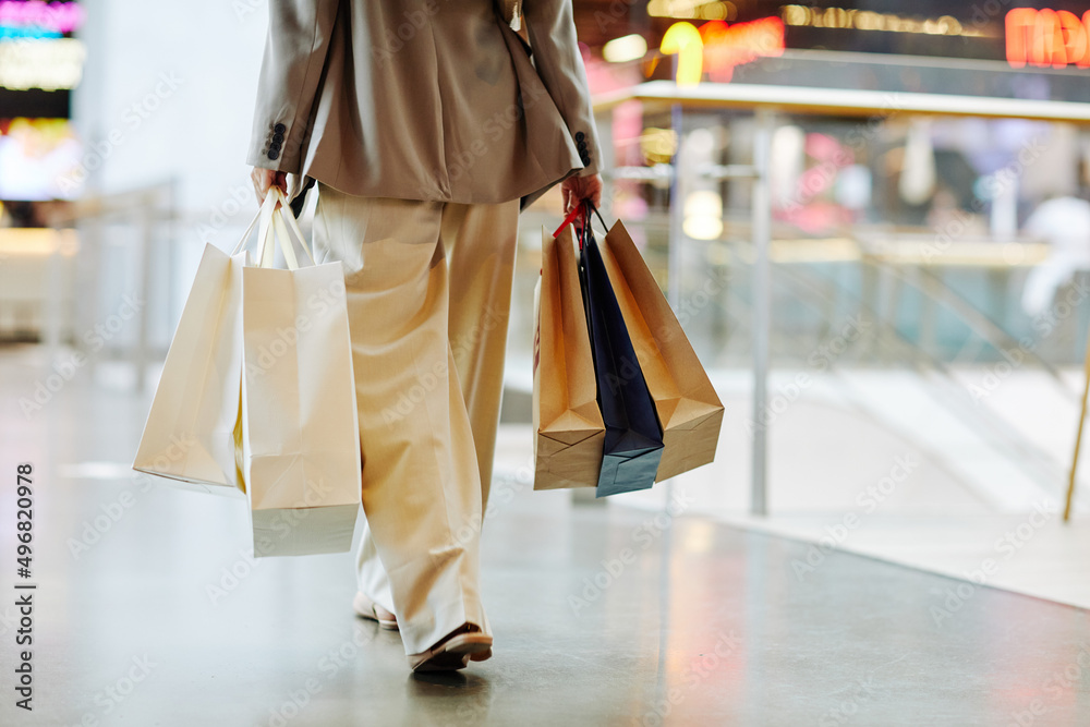 Low section of unrecognizable woman wearing pants and holding blank shopping bags while walking in mall, copy space - obrazy, fototapety, plakaty 