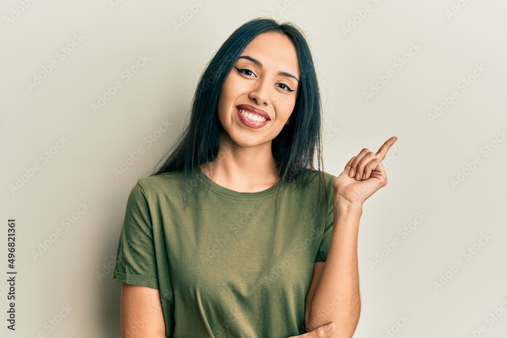 Young hispanic girl wearing casual t shirt with a big smile on face, pointing with hand and finger to the side looking at the camera. Young hispanic girl wearing casual t shirt with a big smile on face, pointing with hand and finger to the side looking at the camera.