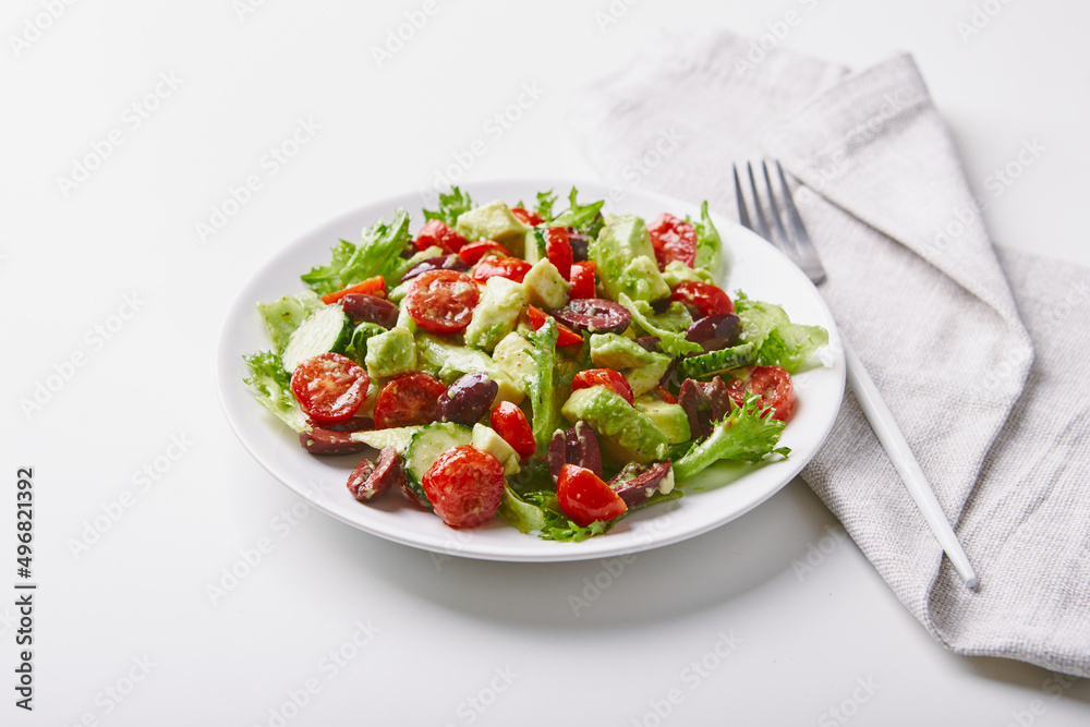 Salad with lettuce, cucumbers, tomatoes, olives and avocados in white plate on the table Salad with lettuce, cucumbers, tomatoes, olives and avocados in white plate on the table