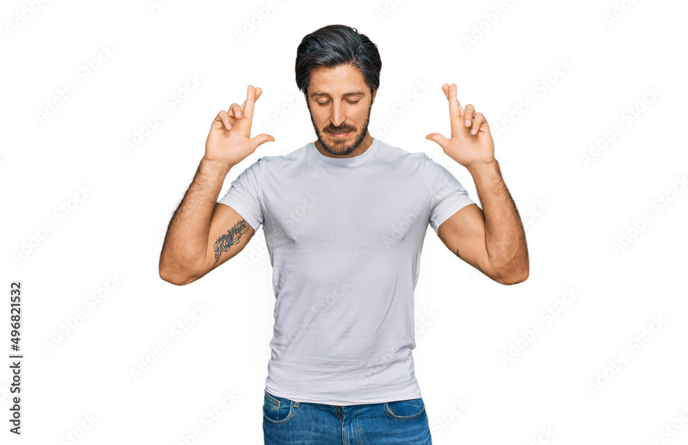 Fototapeta premium Young hispanic man wearing casual white t shirt gesturing finger crossed smiling with hope and eyes closed. luck and superstitious concept.