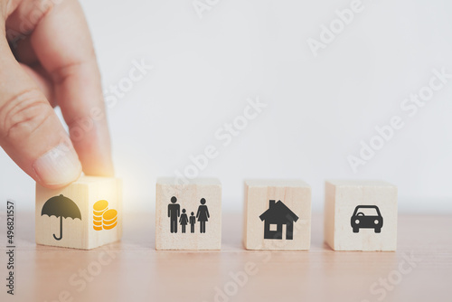 senior's hand flip wooden cube block screen coin to umbrella icon with family, house and car symbol for insurance concept