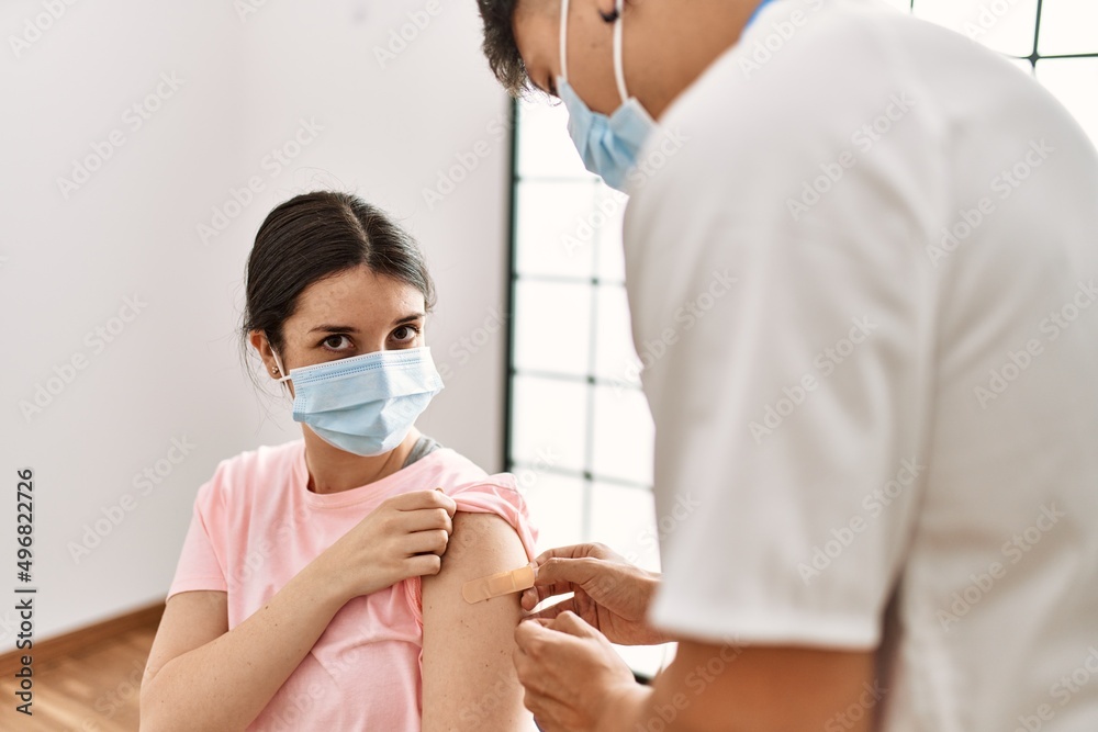 Young nurse man putting band aid on woman arm at the clinic.
