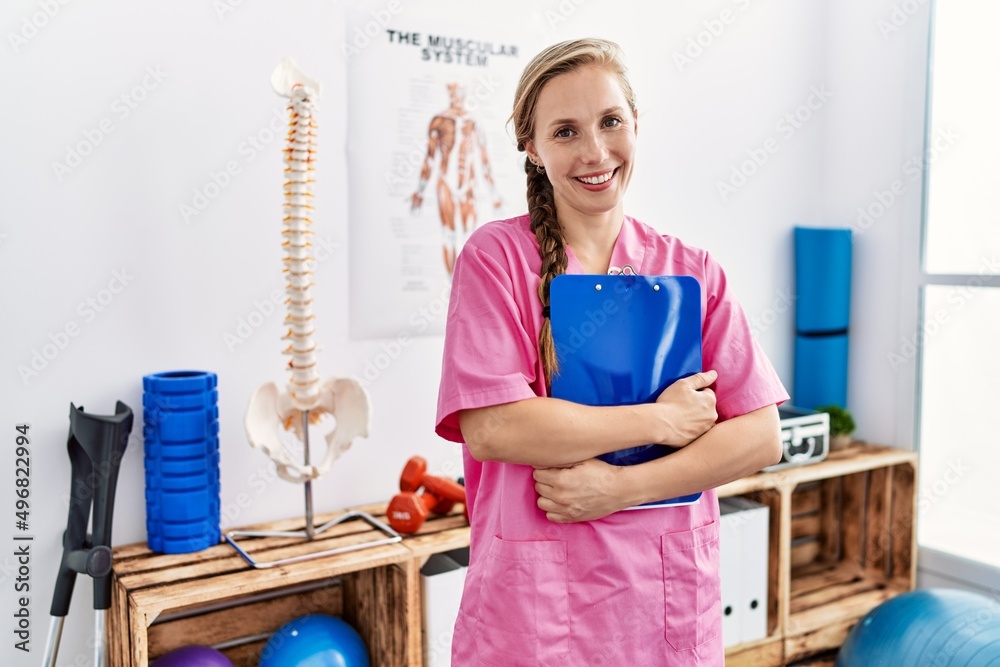 Young caucasian woman wearing physiotherapist uniform holding checklist standing at physiotherapy clinic Young caucasian woman wearing physiotherapist uniform holding checklist standing at physiotherapy clinic