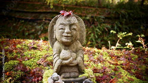 Photography Closeup of a stone statue of a smiling Jizo Bosatsu holding a cat in the park