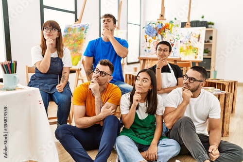 Group of people sitting at art studio serious face thinking about question with hand on chin, thoughtful about confusing idea