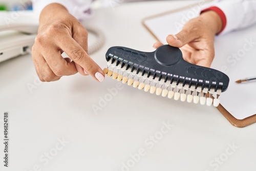 Middle age hispanic woman dentist holding whitening teeth test at clinic