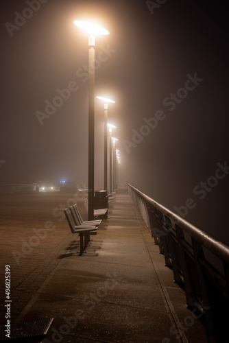 Fototapeta Vertical shot of the city street covered with fog with benches under the street