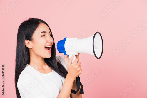 Portrait of happy Asian beautiful young woman teen confident smiling face holding making announcement message shouting screaming in megaphone, studio shot isolated on pink background, with copy space