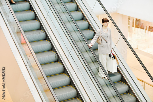 Graphic wide angle view at smart young woman going down escalator in shopping mall and holding bags, copy space