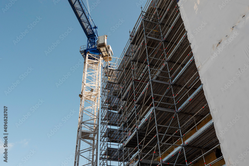 Tall crane and scaffolding by a new modern office of residential building. Construction industry. Blue sky background