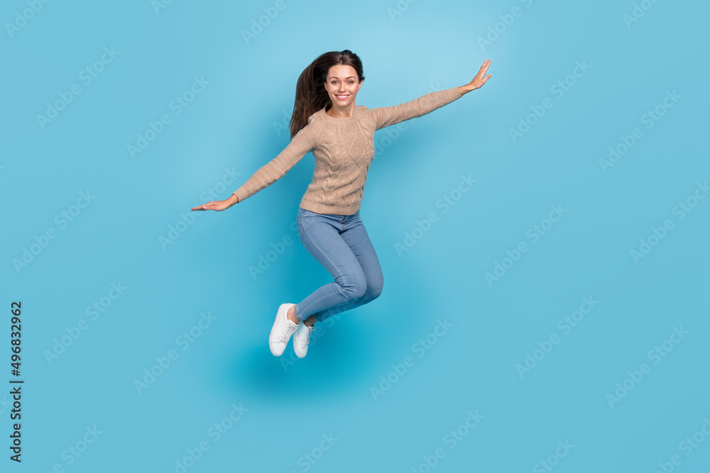 Photo of cheerful nice lady jump raise hands wear beige sweater jeans sneakers isolated blue color background