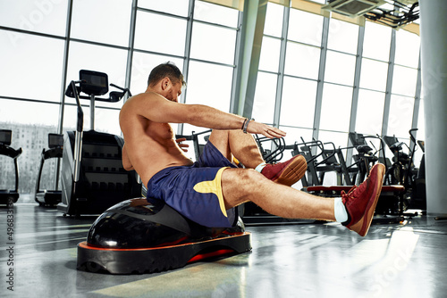 Handsome muscular men works out on functional training soft platform on a background of gym.