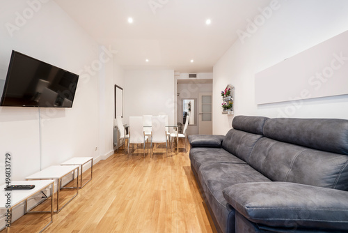 Living room with three-seater gray leather sofa  tv on the opposite wall and wooden floors and white coffee tables