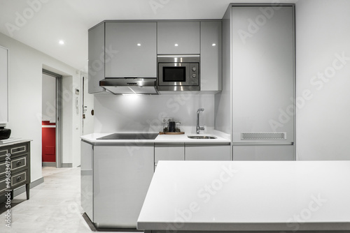 Large kitchen with appliances with smooth gray furniture and stainless steel appliances, white stone countertop and island of the same material