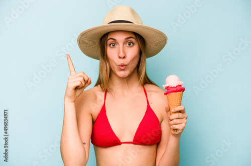 Young caucasian woman wearing a bikini and holding an ice cream isolated on blue background having some great idea, concept of creativity.