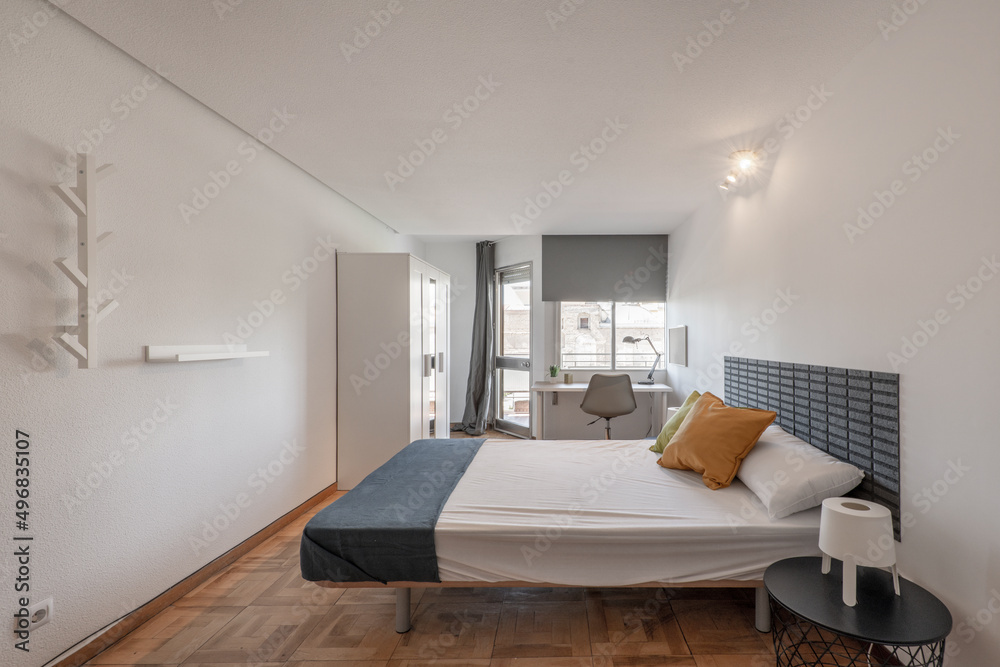 Bedroom with king size bed, circular wooden nightstands, white wooden desks under the window and matching white wooden wardrobe
