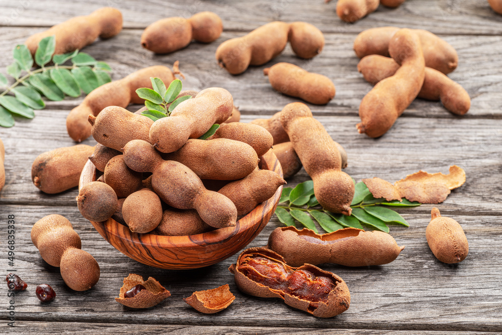 Obraz premium Ripe tamarind fruit, leaves and some tamarind seeds on wooden table.