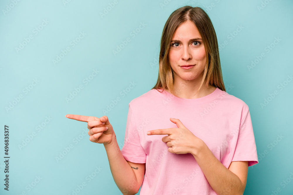 Young caucasian woman isolated on blue background shocked pointing with index fingers to a copy space.
