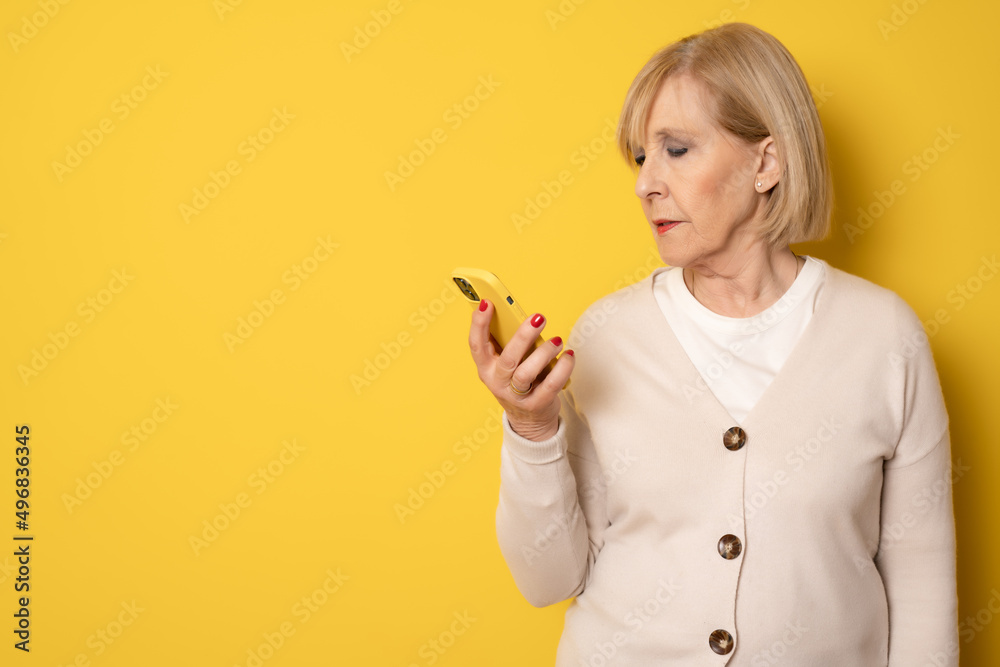 Elderly smiling happy woman 70s in casual clothing talk speak on mobile cell phone isolated on yellow background studio portrait. People lifestyle concept. Elderly smiling happy woman 70s in casual clothing talk speak on mobile cell phone isolated on yellow background studio portrait. People lifestyle concept.