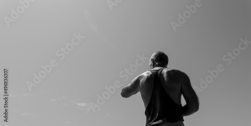 Monochrome of rear view of adult man on beach against sunny sky.