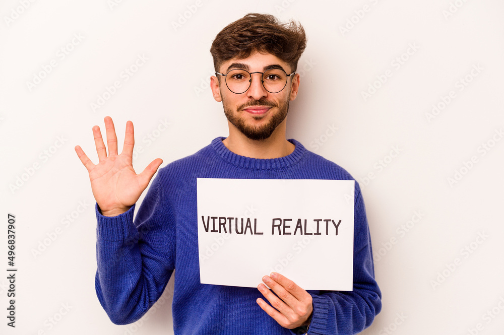 Young hispanic man holding a virtual reality placard isolated on white background smiling cheerful showing number five with fingers. Young hispanic man holding a virtual reality placard isolated on white background smiling cheerful showing number five with fingers.