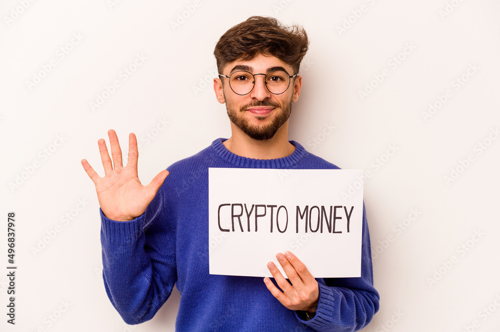 Young hispanic man holding a crypto money placard isolated on white background smiling cheerful showing number five with fingers. Young hispanic man holding a crypto money placard isolated on white background smiling cheerful showing number five with fingers.