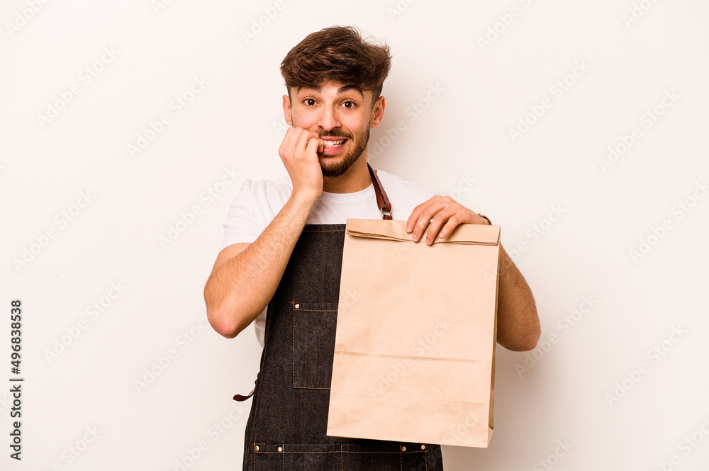 Young hispanic clerk man holding a take away bag isolated on white background biting fingernails, nervous and very anxious. Young hispanic clerk man holding a take away bag isolated on white background biting fingernails, nervous and very anxious.